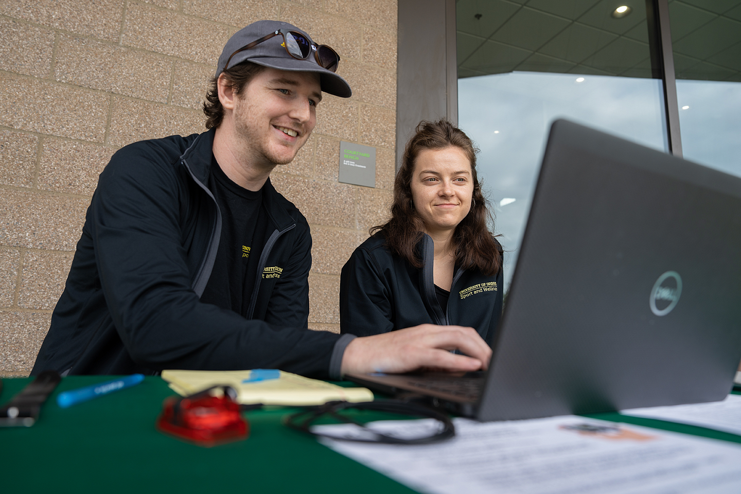 Researchers Zach Farley and Esmeralda Castro study data on a laptop outside the Kidsports facility