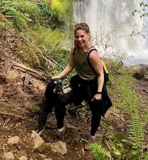 Alaina Burgess hiking with her dog, Gus, a Schnauzer-type, with a waterfall in the background