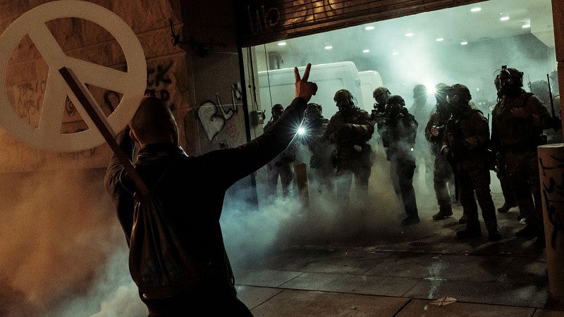 Protester with peace sign stands in front of police force amid smoke and dark lighting