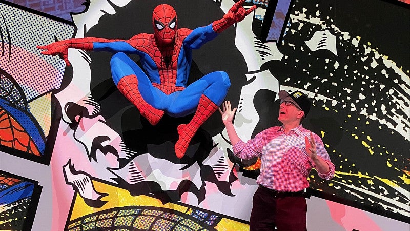 Ben Saunders gestures at a a life-sized Spider-Man figure at a museum exhibit