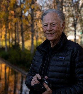 Alumnus photographer Michael Wilkes, framed against a backdrop of fall leaves and shimmering water