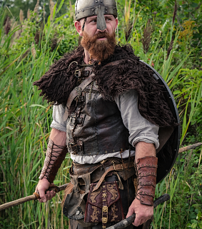 Thorfinn, in full battle gear, looks intensely against a forest backdrop