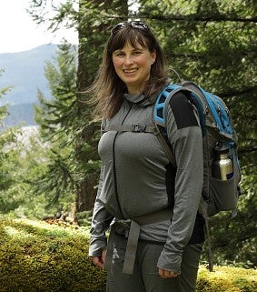 Chandra LeGue during a hike, wearing a backpack and backed by evergreen trees and a ridge
