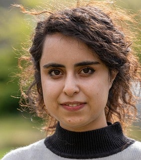 Saghar Salehi portrait, in striped top and trees, grass in background