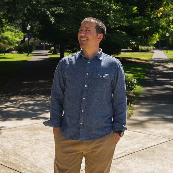 Raoul Liévanos walking on tree-lined campus, smiling amid a sunny day