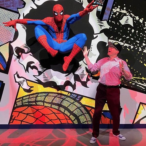Ben Saunders gestures at a a life-sized Spider-Man figure at a museum exhibit