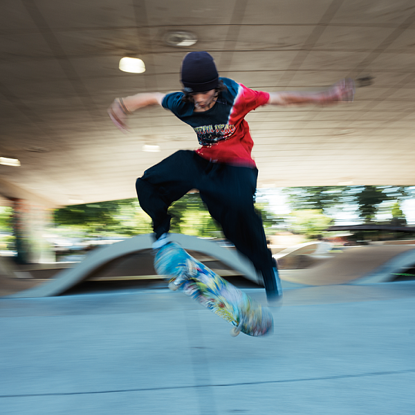 Youth on skateboarding does flip-board trick against urban backdrop