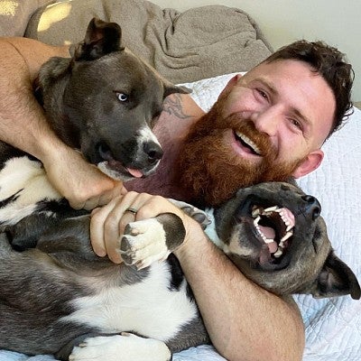Devan Long curls up, laughing, with two dogs that look like pit bulls